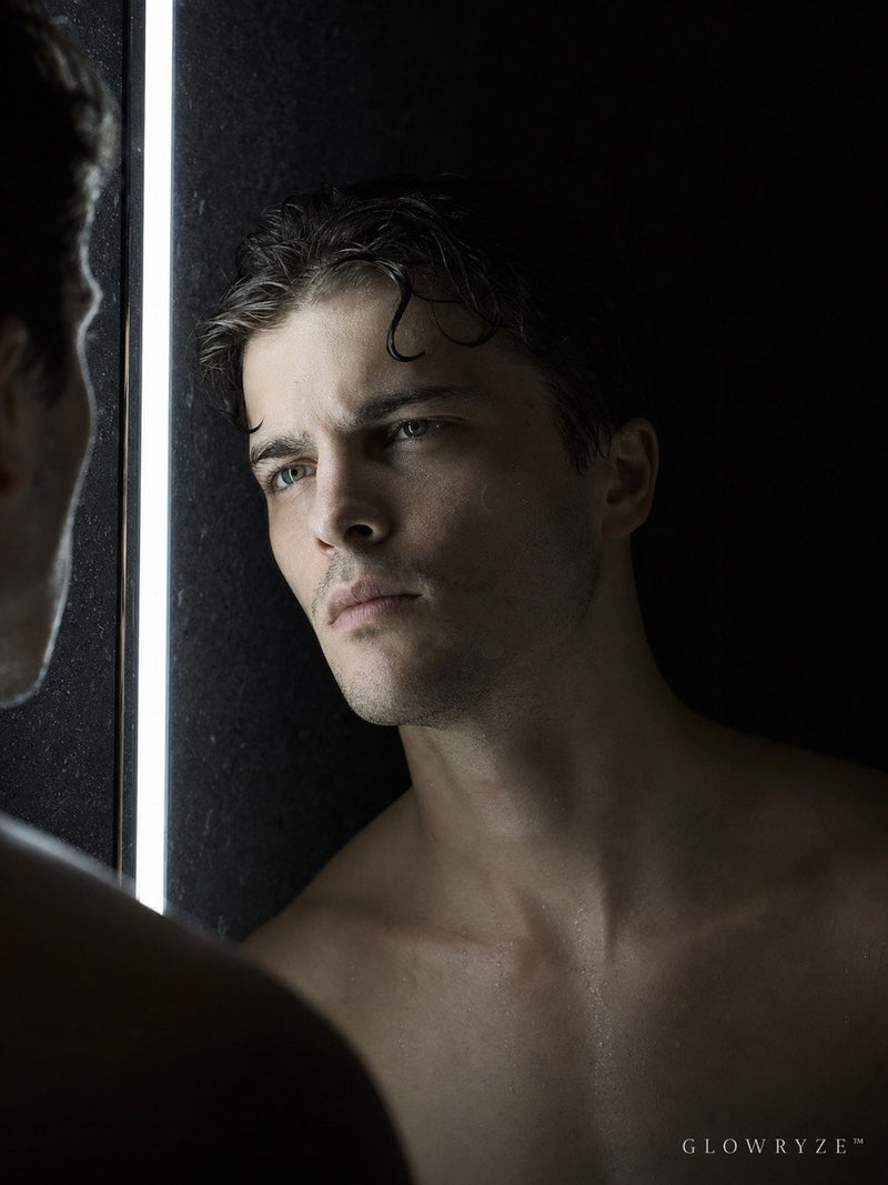 Man checking his reflection during his morning skincare routine in a dimly lit bathroom